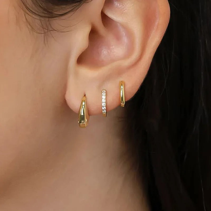 Close-up of an ear wearing gold hoop earrings with a blurred background