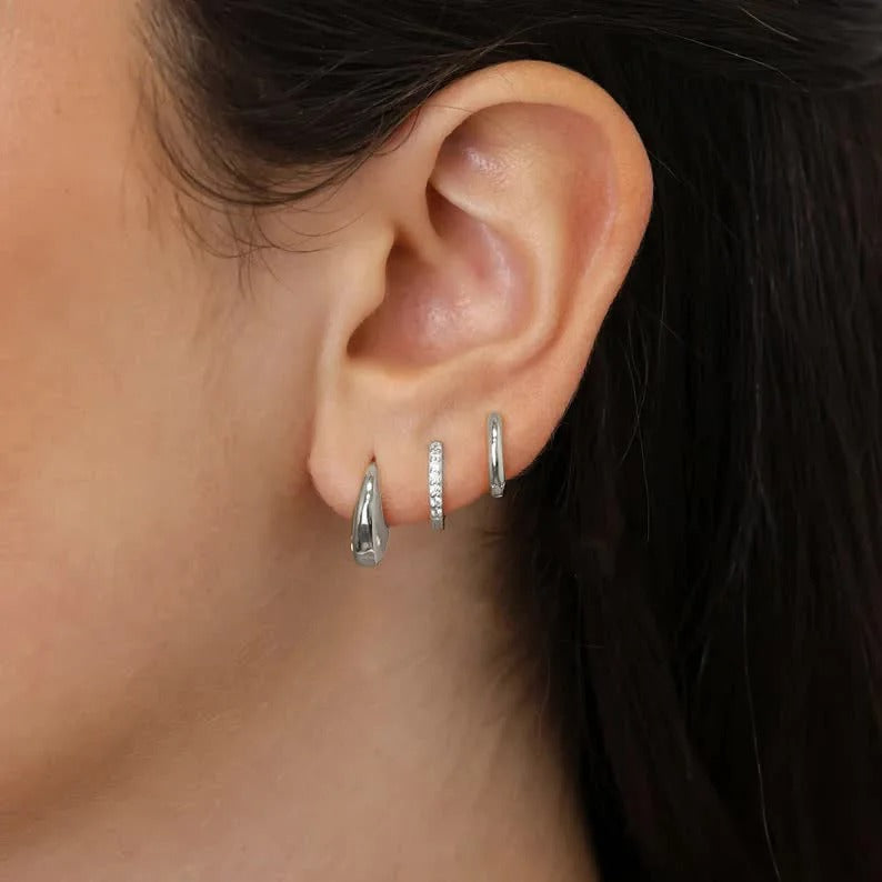 Close-up of an ear wearing silver hoop earrings with a blurred background