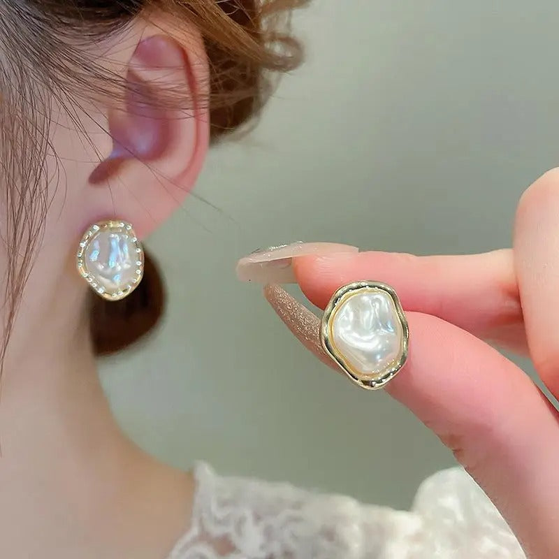 Pearl earrings being held up to a person's ear against a neutral background