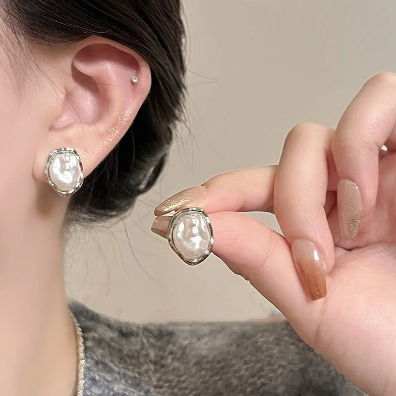 Pearl earrings being worn and held by a person against a neutral background