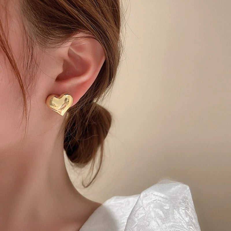 Gold heart-shaped earring worn by a person with a neutral background