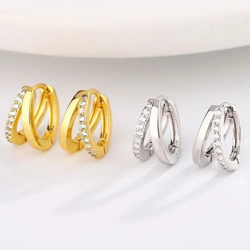 Three pairs of small hoop earrings displayed on a clean white surface. The left pair is yellow gold with clear stones along one band, the center pair is silver-toned with clear stones along one band, and the right pair is plain silver-toned.