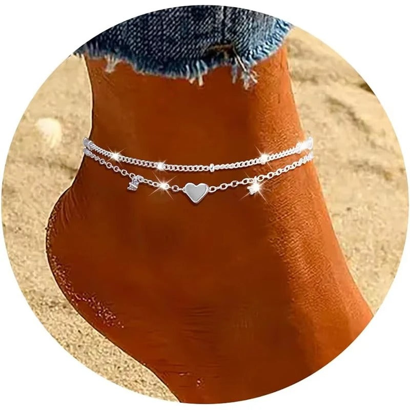 Silver anklets with heart charm on a person's ankle against a neutral background